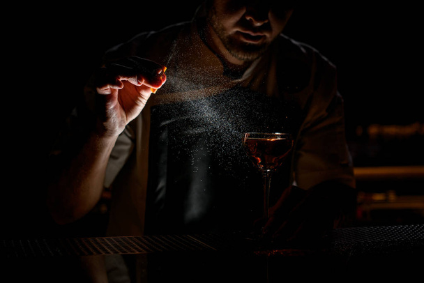 Barista professionista che spruzza sulla bevanda alcolica marrone con un succo di scorza d'arancia al buio
 - Foto, immagini