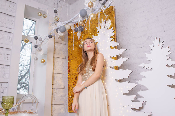 girl in a shiny evening dress. Christmas Eve. Cozy holiday at the fur-tree with lights and gold decor - Fotografie, Obrázek