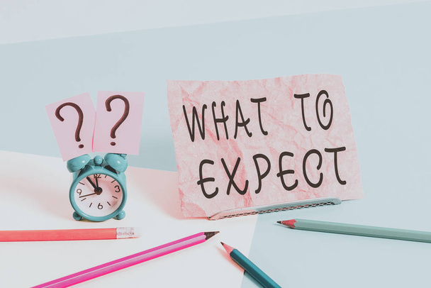 Conceptual hand writing showing What To Expect. Business photo showcasing Confusion about the belief of what will happen in future Mini size alarm clock beside stationary on pastel backdrop. - Photo, Image
