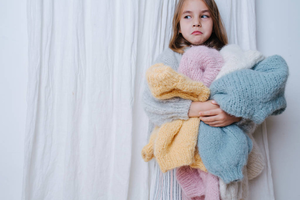 Upset little girl with a pile of soft freshly washed sweaters doing chores - Foto, Bild