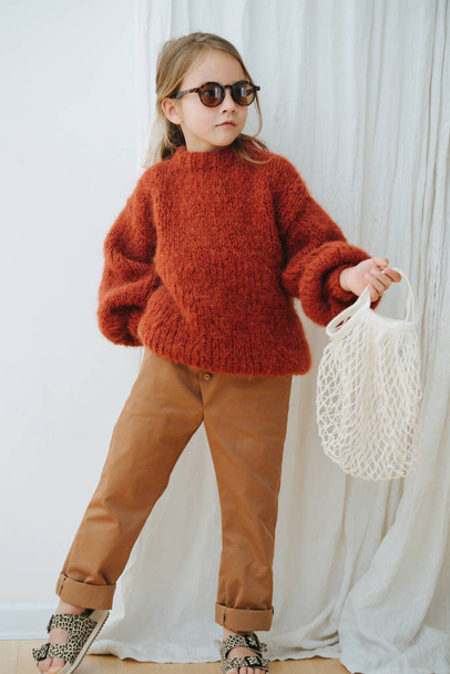 Fashionable little girl in dark orange knitted sweater with net bag - Foto, afbeelding