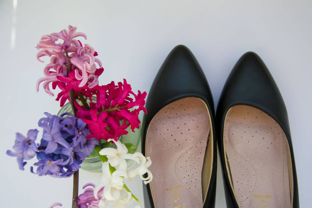 Close-up of black female shoes, high heels on white background with hyacinth flowers in a vase, feminine concept - 写真・画像