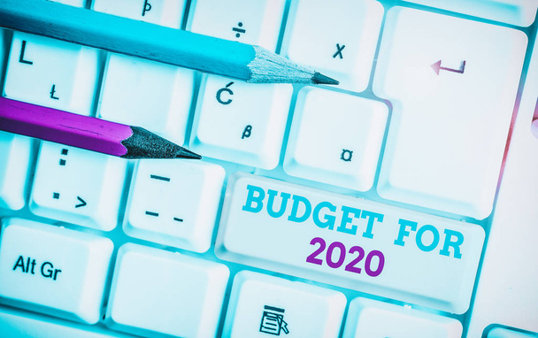 Schreibnotiz mit Haushaltsplan für 2020. Geschäftsfoto, das eine schriftliche Schätzung der Einnahmen und Ausgaben für 2020 zeigt, weiße PC-Tastatur mit Notizpapier über weißem Hintergrund. - Foto, Bild