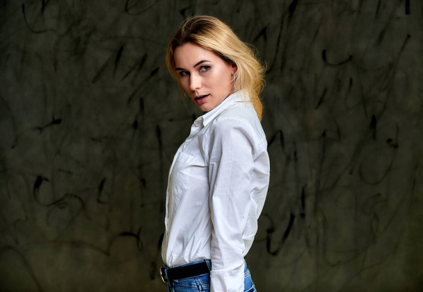 Portrait of a pretty smiling blonde woman in a white shirt with flying hair standing on a gray alternative background. Right in front of the camera with emotions. - Foto, Imagem