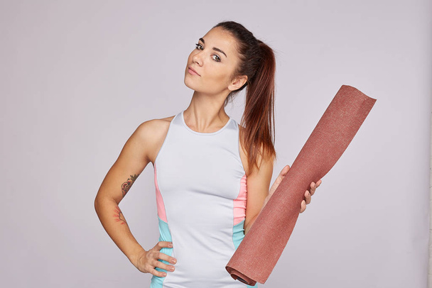 Sporty energetic athletic Caucasian woman wears slim sports top smiles at camera, likes sport and active lifestyle, poses against grey studio background. People, health and physical activity concept. - Photo, Image