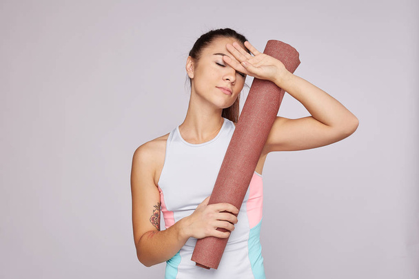 Tired fitness woman feels exhausted, keeps hand on forehead, feels fatigue after aerobic and hard training in gym, dressed in sportswear, poses against grey background. People, sport and determination - Foto, imagen