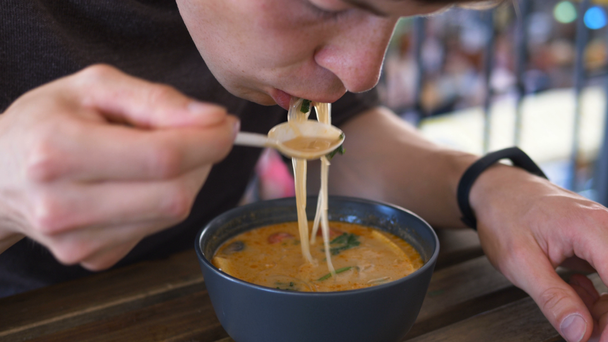 man tastes soup in black bowl sitting at brown cafe able - Video, Çekim