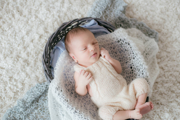 Cute little baby lies at home on a white fluffy carpet in a wicker basket with soft knitted plaids. Happy motherhood - Photo, image