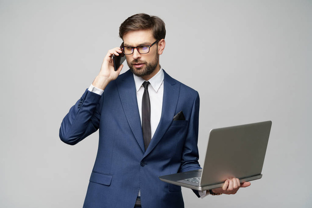 businessman talking on the phone and holding laptop isolated over grey background - Photo, Image