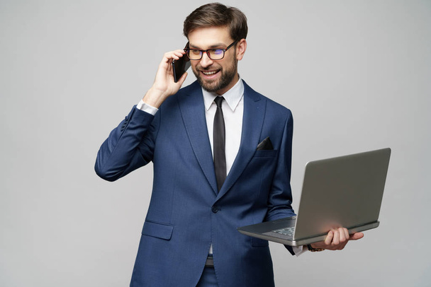 uomo d'affari parlando al telefono e tenendo il computer portatile isolato su sfondo grigio
 - Foto, immagini