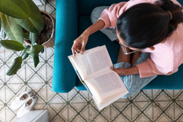 Гарненька молода жінка читає книгу, сидячи на дивані вдома
. - Фото, зображення