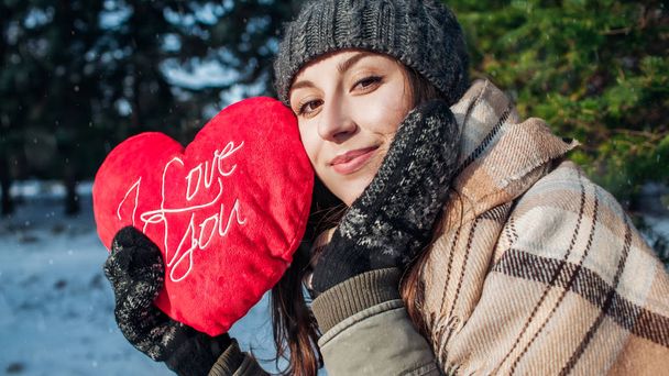 Valentin nap. Fiatal nő tartja piros párna szív alakú I love you writing in winter forest - Fotó, kép