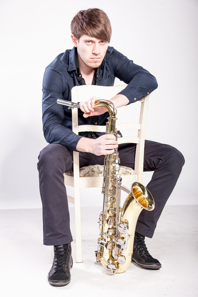 Музыкант сидит на стуле и держит саксофон
 - Фото, изображение