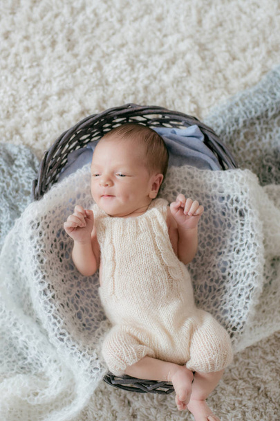Lindo bebé se encuentra en casa en una alfombra mullida blanca en una canasta de mimbre con suaves cuadros de punto. Feliz maternidad.
 - Foto, imagen