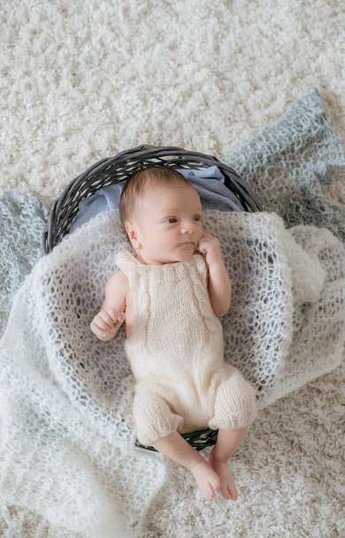 Şirin küçük bebek yumuşak örülmüş ekoseli sepetin içinde beyaz bir halının üzerinde uzanıyor. Mutlu annelik - Fotoğraf, Görsel