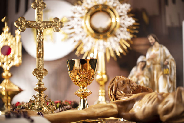 Tema Iglesia Católica Romana. La Cruz, la Santa Biblia, la monstrancia, el rosario y el cáliz dorado sobre una mesa rústica de madera
 - Foto, imagen