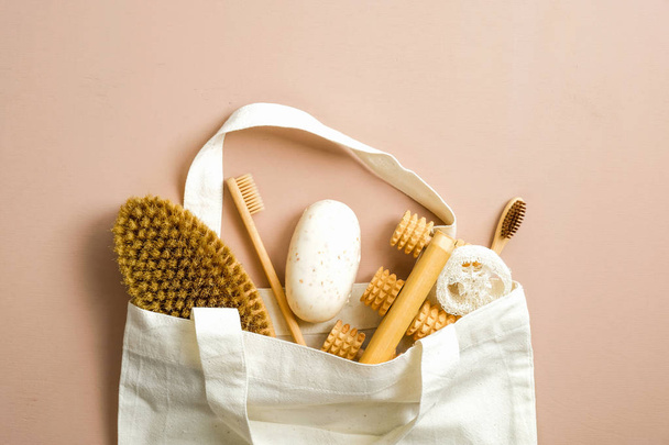 Flat lay Eco friendly bathroom tools in fabric canvas shopper bag on brown background. Top view luffa sponge, spa brush, homemade soap, bamboo toothbrushes. Zero waste, plastic free concept. - Fotó, kép