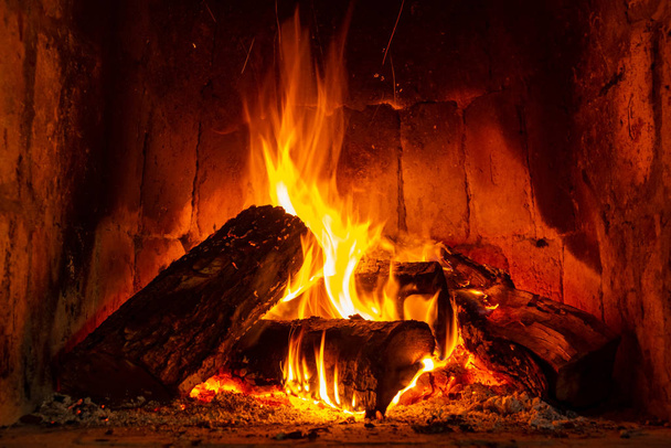Tűz a kandallóban, rönkökkel és lángokkal, melegséget és meghittséget keltve.. - Fotó, kép