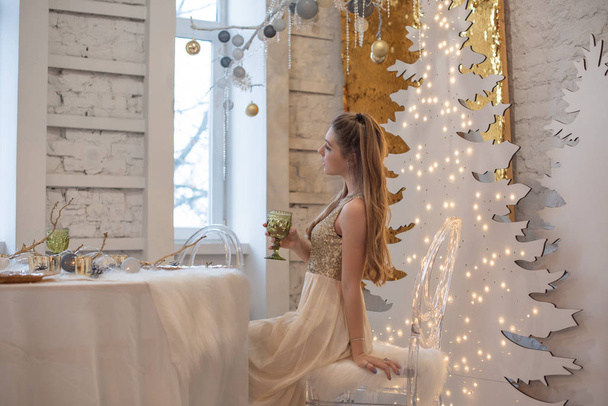 Parlak bir gece elbisesi giyen kız. Noel arifesi. Kürk ağacında rahat bir tatil Işıklar ve altın dekorla - Fotoğraf, Görsel