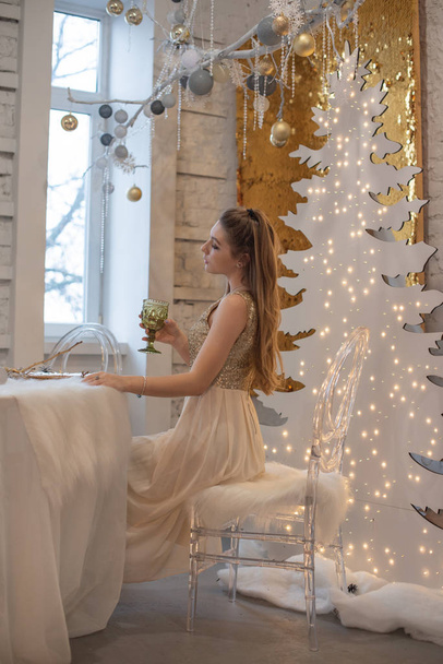 Parlak bir gece elbisesi giyen kız. Noel arifesi. Kürk ağacında rahat bir tatil Işıklar ve altın dekorla - Fotoğraf, Görsel