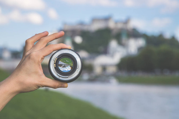 Hand holding camera lens with old city of Salzburg in it, close up - Foto, Imagen