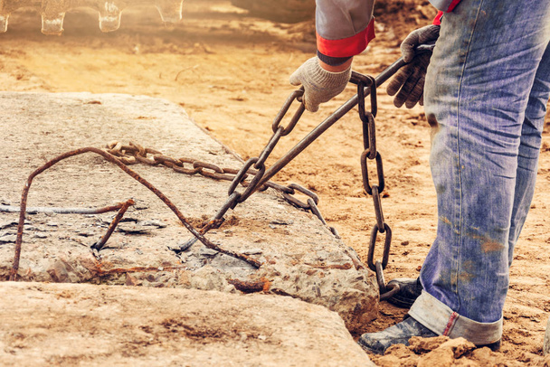 El trabajador agarra cadenas en el cubo de la excavadora para transportar e instalar losas de hormigón en la carretera
. - Foto, Imagen