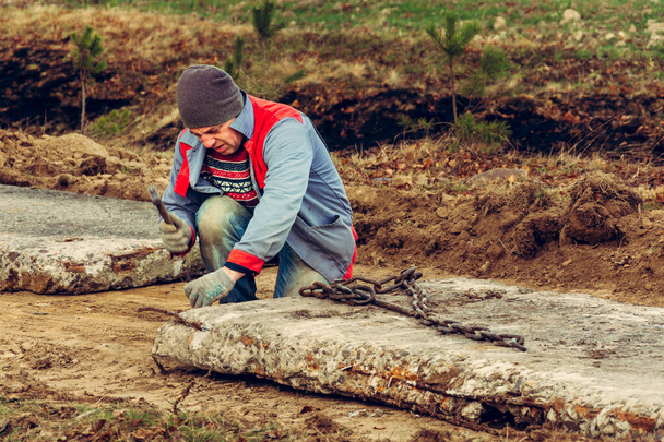 İşçi, kazıcının kovasıyla taşıdığı beton levhaların zincirlerini çözer.. - Fotoğraf, Görsel
