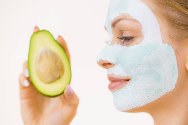 Girl facial mud mask holds avocado fruit - Valokuva, kuva