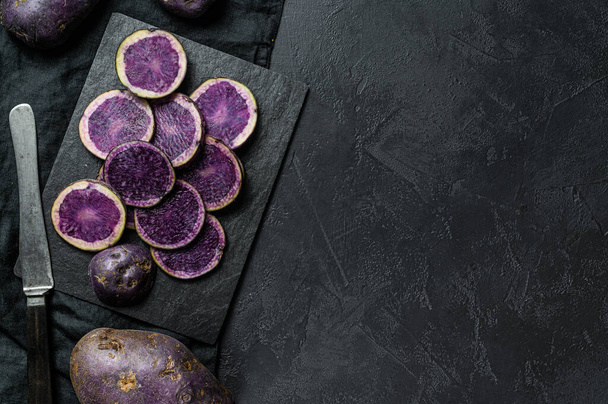 Raakaa viipaloitua violettia perunaa. Musta tausta. Huippunäkymä. Tekstitila
 - Valokuva, kuva