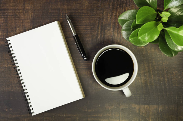 Top view of open school notebook with blank pages, Pen, Plant and Coffee cup on wooden table background. Business, office or education concept with copy space. - Photo, image