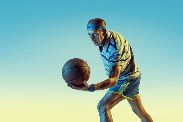 Senior man playing basketball in sportwear on gradient background and neon light - Photo, image