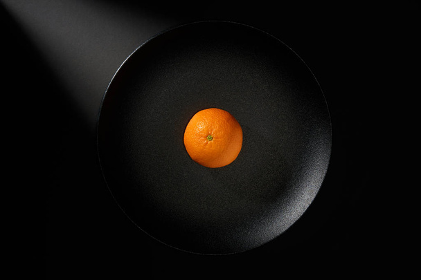 Tangerine in black plate on black background with ray of light   - 写真・画像