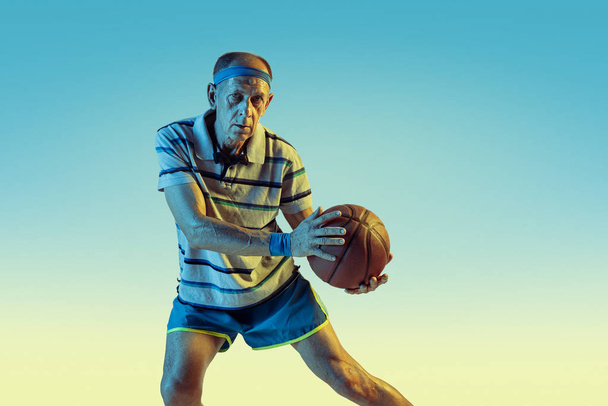 Senior man playing basketball in sportwear on gradient background and neon light - Foto, imagen