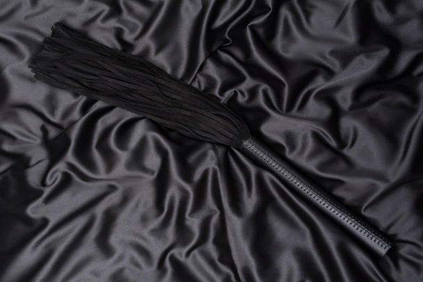 黒い絹の背景に黒い鞭。大人の性的ゲームのためのアクセサリー。ジェムのおもちゃ - 写真・画像