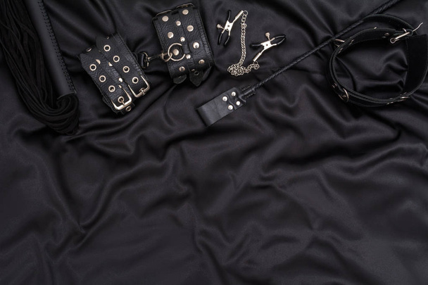 Menottes en cuir, fouet noir, col chaîne et pile sur fond noir. Accessoires pour jeux sexuels pour adultes. Tenue BDSM
. - Photo, image