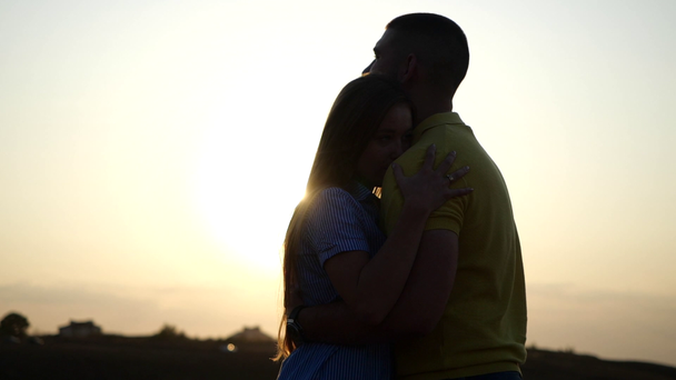 Silhouette di un giovane barbuto e della sua ragazza che si abbracciano, si abbracciano e si baciano. Giovane coppia affascinante che si tiene per mano baciando nel paesaggio rurale al tramonto
. - Filmati, video
