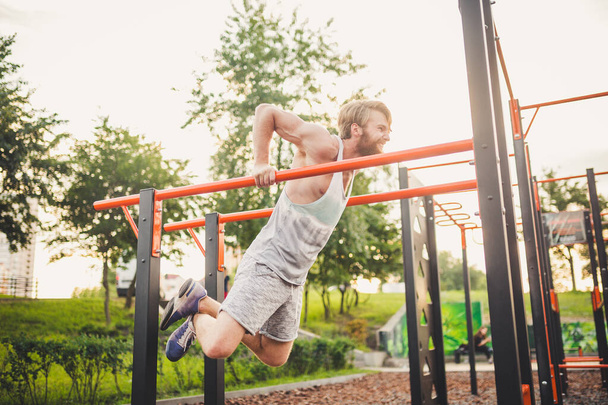 Fit Man Workout Out Arms On Dips Horizontal Bars Training Triceps And Biceps Doing Push Ups. Handsome Man Doing Exercise On Parallel Bars. Male Athlete Exercises On Parallel Bars Outdoor - Фото, зображення