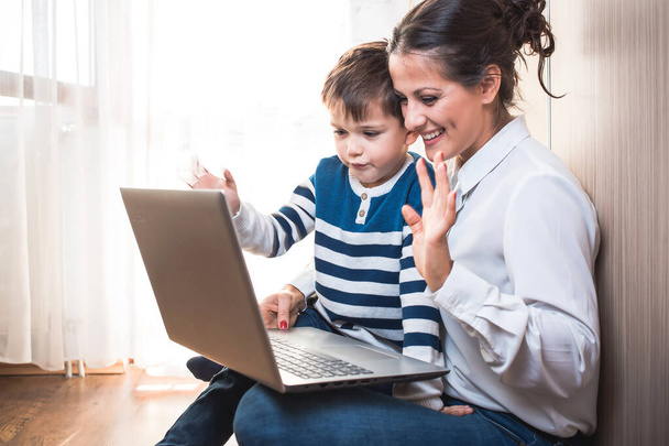 Beautiful young mom and her son looking at laptop and waving. Video call - Foto, Bild