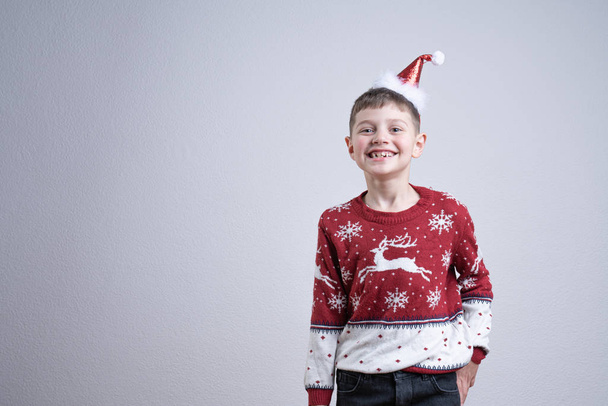 Feliz niño sonriente en suéter rojo de santa y sombrero mirando a la cámara, aislado sobre fondo gris, Feliz Navidad y Feliz Año Nuevo concepto
 - Foto, imagen