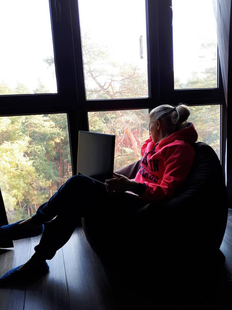giovane ragazza bionda a casa a lavorare su un computer portatile e parlare al telefono vicino a una grande finestra
 - Foto, immagini
