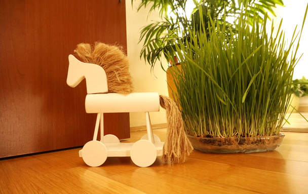 Detalle de decoración del hogar. Juguete de caballo de madera en el suelo de madera con hierba verde por la derecha
 - Foto, imagen