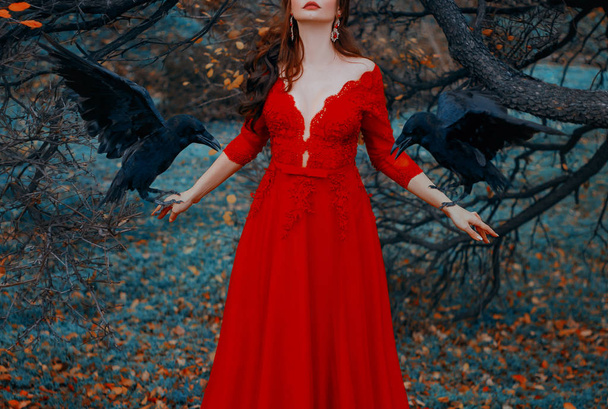Mysterious woman with red lips in a luxurious dress with a seductive deep neckline. Witch conjures summons black ravens. Glamorous lady with birds. Autumn fairytale landscape. Shooting without a face. - Foto, Bild