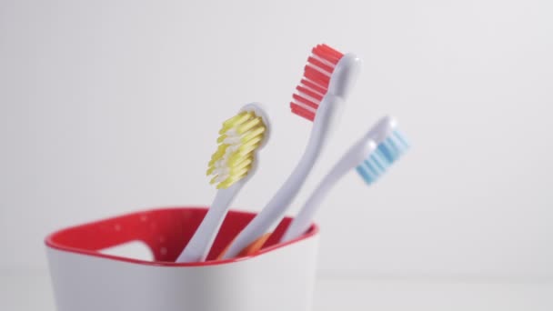 Um jovem puxa uma escova de dentes com cerdas vermelhas de um copo de plástico no banheiro para higiene pessoal e limpeza dos dentes
 - Filmagem, Vídeo