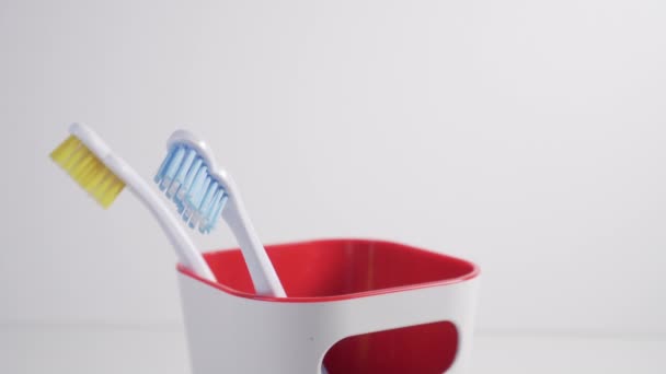 Um jovem coloca uma escova de dentes com cerdas vermelhas em um copo de plástico no banheiro após a higiene pessoal e a limpeza dos dentes
 - Filmagem, Vídeo