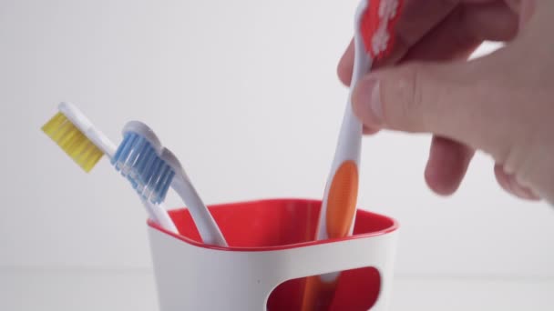 Cepillos de dientes azules y amarillos en una taza de plástico. El joven añade rojo. Productos de higiene personal en la familia
 - Imágenes, Vídeo