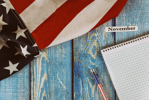 Νοέμβριος μήνα του ημερολογιακού έτους Ηνωμένες Πολιτείες της Αμερικής σημαία του συμβόλου της ελευθερίας και της δημοκρατίας με κενό σημειωματάριο και στυλό στο γραφείο ξύλινο τραπέζι - Φωτογραφία, εικόνα