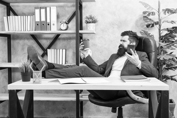 Mobile call. Start day with coffee. Coffee relaxing break. Man bearded businessman hold cup and smartphone. Coffee is pledge of successful negotiations. Caffeine addicted. Boss enjoying energy drink - Fotografie, Obrázek