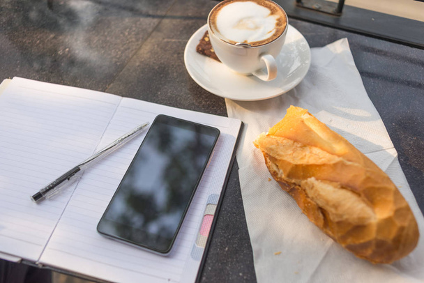 スマートフォン、ホットコーヒー、パンで朝の作業日 - 写真・画像