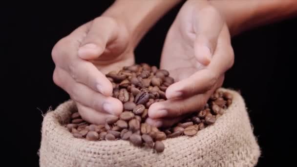 Roasted coffee beans falls down from hands on a black background - Séquence, vidéo