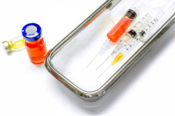 Vacuna en viales y jeringas de plástico con agujas médicas colocadas en un recipiente médico de acero inoxidable para inyección lista para el paciente sobre fondo blanco
. - Foto, Imagen
